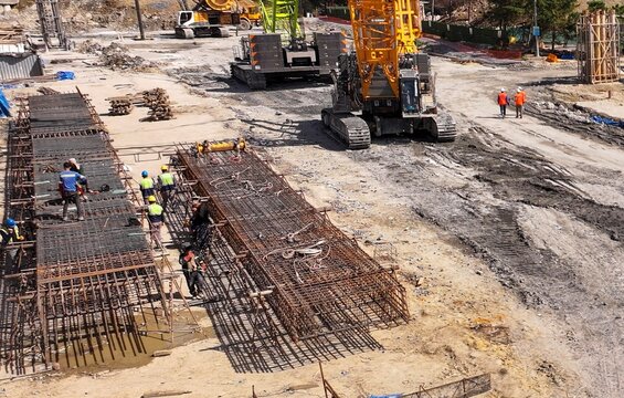 Aerial view of construction workers assembling steel rebar cages near heavy machinery and cranes at a building site in Avcilar, Istanbul, Turkiye.