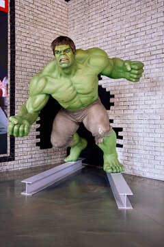 Life-size Incredible Hulk statue crashing through a brick wall, stepping on steel I-beams in a comic book or movie display.