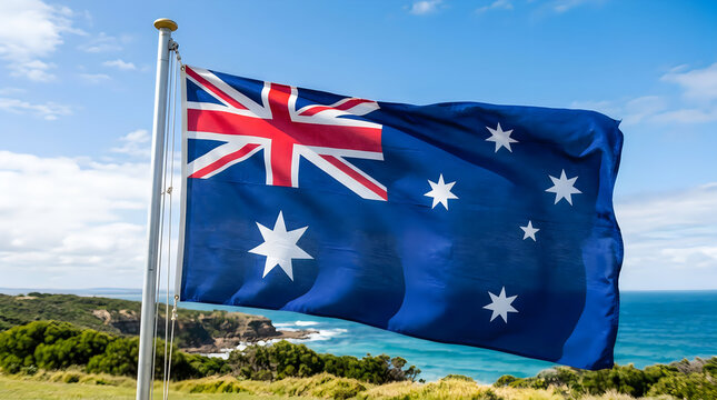 Australian flag waving strongly near coastal landscape with clear blue sky