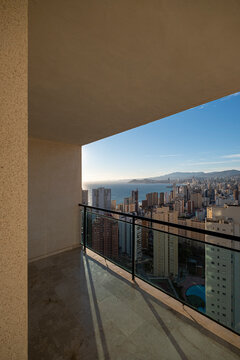 Wide Benidorm Spain terrace frames Mediterranean sea, balcony railing, skyline towers and distant mountains through angular architecture