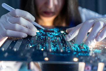 A scientist is focusing on a circuit board, using a tool to make adjustments in a laboratory setting