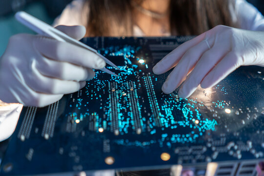 A technician observes a circuit board while using a tool to inspect details in the laboratory at night
