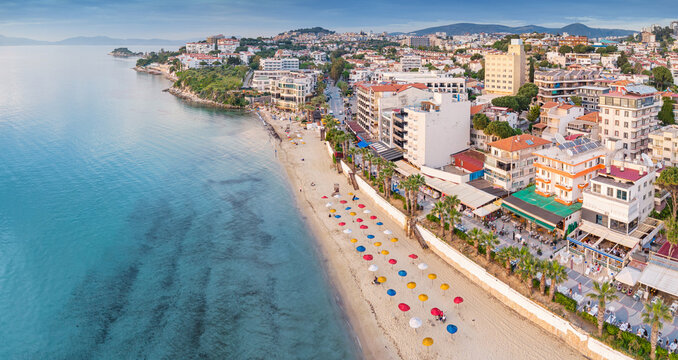 Kusadasi, Turkey, featuring a vibrant beach with colorful umbrellas and resort buildings along the Aegean Sea coast