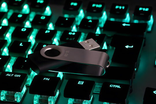 Gros plan d&rsquo;une cl&eacute; USB m&eacute;tallique de 16 Go pos&eacute;e sur un clavier m&eacute;canique d&rsquo;ordinateur r&eacute;tro&eacute;clair&eacute; en turquoise. Concept de stockage de donn&eacute;es, sauvegarde informatique, transfert de fichiers, cyber