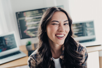 Obraz premium Smiling female programmer winking in a bright home office surrounded by laptops and monitors showing code, conveying confidence, creativity and a friendly modern remote work lifestyle