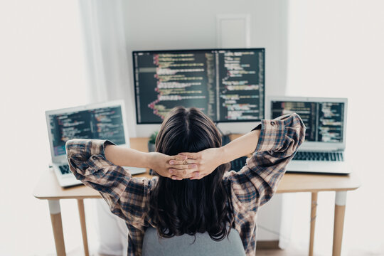 Female programmer relaxing in a home office surrounded by laptops and monitors with code on screen, remote developer taking a break while working on software development projects
