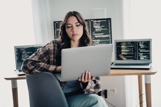 Woman programmer working on multiple laptops coding at a home desk, focused software developer and remote worker reviewing code on screens