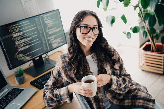 Smiling programmer at home office desk coding on dual monitors while enjoying a coffee break