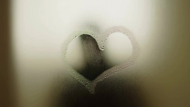 Heart shape drawn on a foggy glass surface. Symbolizes love, connection, and intimacy in a romantic setting