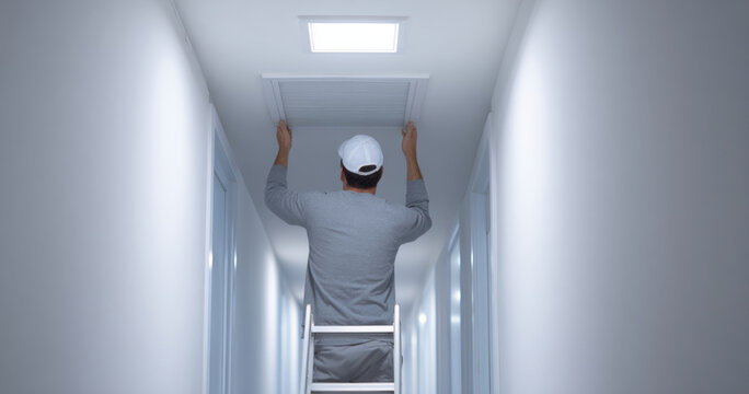 Technician Inspecting Ceiling Vent in Hallway