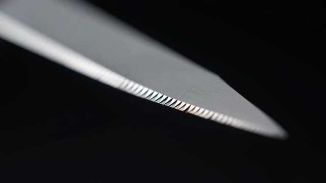 Macro shot of a sharp serrated metal knife blade edge on black background.