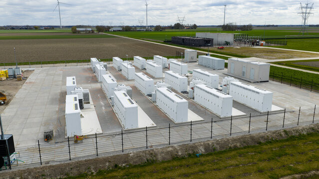 Aerial view of rows of white battery storage containers at a renewable energy facility with wind turbines and green fields in the background Dronten, Flevoland, Netherlands.