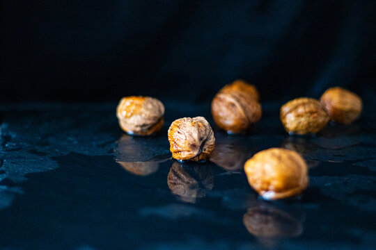 Close-up of whole walnuts in shells on a wet dark surface with water reflections

