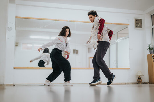 Two young dancers perform synchronized contemporary moves in a bright studio space. The pair rehearse choreography together in front of a large wall mirror