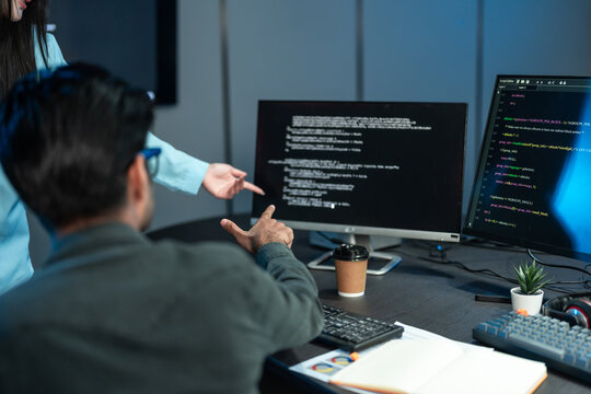 Developers Pointing At Code On Monitor In Dark Office