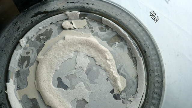 Close up of thick limescale and calcium deposits on the bottom of an old used kettle. Background texture of hard water scale buildup, mineral corrosion and damage inside electric boiler pot.