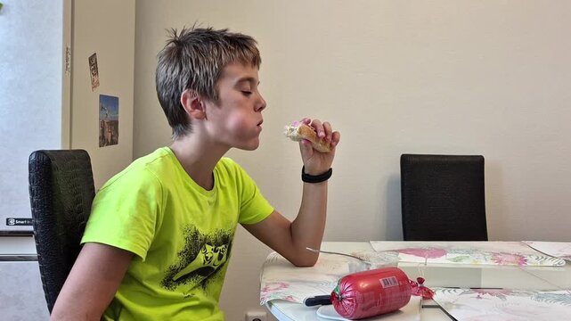 A teenage boy eats a sandwich with gusto, chews, and squints with pleasure
