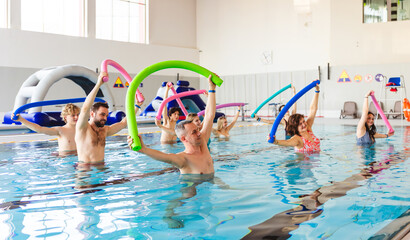 Fototapeta na wymiar Group of people of various ages participating in an aqua aerobic class in an indoor swimming pool