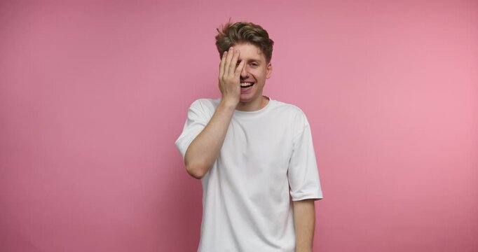 Man laughs and interacts with camera in a studio with pink background during a fun moment in daylight