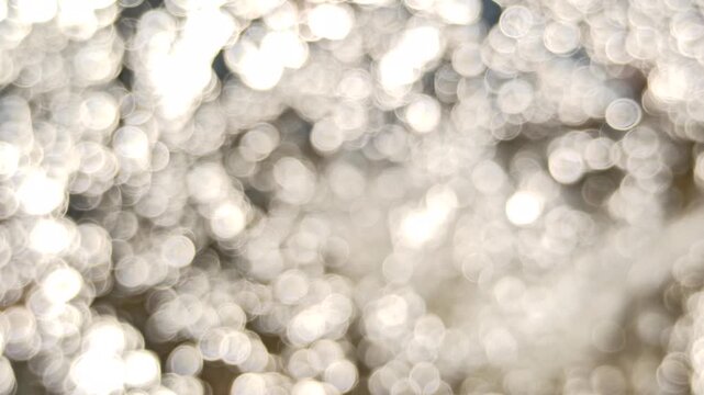 Artistic blur and defocused view of shimmering water ripples under daylight, highlighting sparkling reflections and abstract optical effects on the water surface.