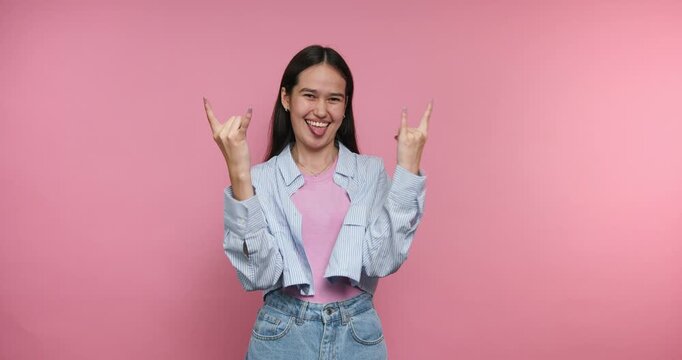 Smiling girl shows hand signs for fun in bright studio with pink background during daytime