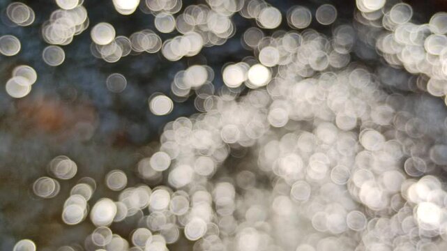 Artistic blur and defocused view of shimmering water ripples under daylight, highlighting sparkling reflections and abstract optical effects on the water surface.