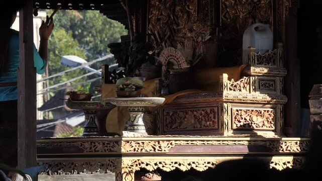 Balinese Hindu offering ceremony, with a woman placing flowers and incense on a ceremonial tray. Rising smoke creates a spiritual atmosphere during a temple ritual in Bali, Indonesia