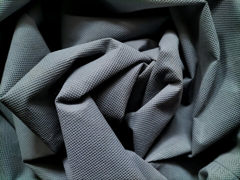 Abstract composition of crumpled grey polypropylene fabric arranged in deep folds. Macro texture of textured nonwoven technical textile material with dramatic lighting.