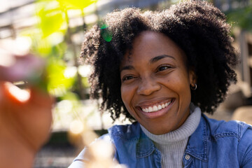 Mid-adult African American woman smiling reaching for green leaves in sunny garden in denim jacket