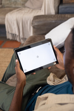 African man sitting on sofa holding tablet, viewing blank screen with calibration markers at home