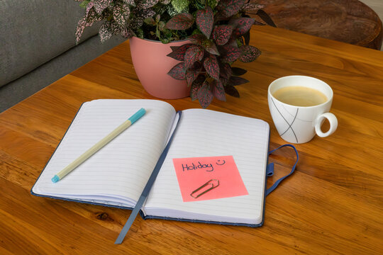 Carnet ouvert avec note vacances et tasse de caf&eacute; sur table en bois