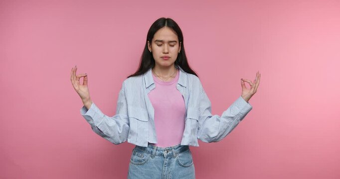 Woman practices meditation in a bright room with a pink wall wearing casual clothes during a calm moment in the day