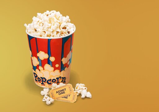 Popcorn bucket with movie tickets and spilled kernels on a yellow background with copy space
