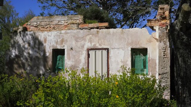 Abandoned old house surrounded by trees in a rural landscape under blue sky. Concept of depopulation, migration, urban decay and deserted villages. High quality 4k footage