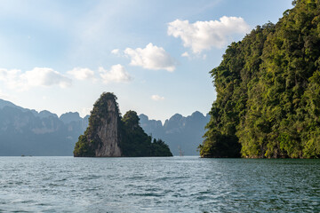 Naklejka premium Dramatic limestone karst islands adorned with lush green jungle rise majestically from the tranquil turquoise waters under a bright blue sky with scattered white clouds.