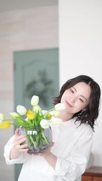 チューリップの花を持って笑顔を見せる女性の丁寧な暮らしのくつろぐライフスタイルイメージの縦動画