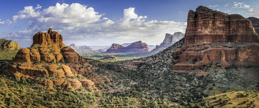 Aerial view of the iconic red rock formations of Bell Rock Trail under a blue sky with scattered clouds in the desert landscape of Sedona, Arizona, United States.