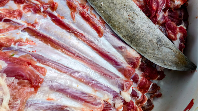 Close-up of fresh goat ribs and a traditional butcher knife during meat processing, ideal for editorial content, cultural articles, educational materials, and livestock industry publications.