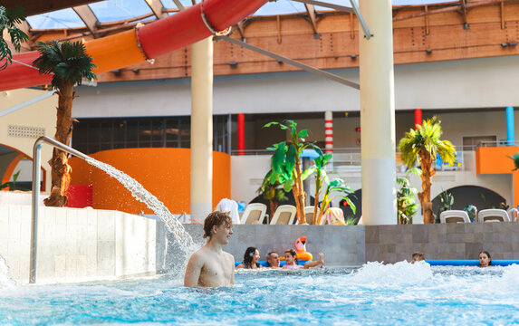 Young man enjoying water spray in an indoor swimming pool of a large water park