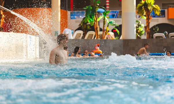 Young man enjoying water spray in an indoor swimming pool of a large water park