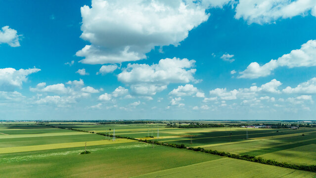 Aerial view of vast green agricultural fields and rural landscape under a bright blue sky with fluffy white clouds in Sremska Mitrovica, Vojvodina, Serbia.
