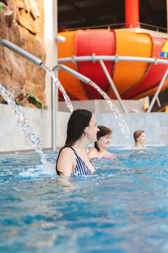 Happy mature woman relaxing with friends under a water fountain in an indoor swimming pool at a water park