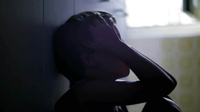 Close view of child holding head with eyes closed showing deep emotional exhaustion depression and trauma conveying inner turmoil and psychological distress in home setting