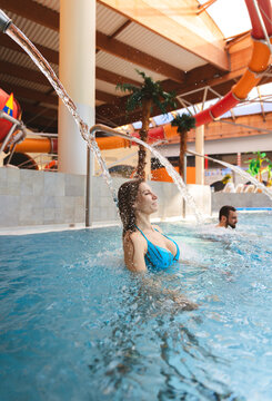 Beautiful young woman smiling and enjoying water spray in an indoor swimming pool of a water park