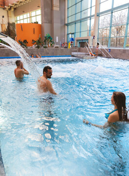 Happy young men relaxing and enjoying water spray from a massage fountain in an indoor swimming pool