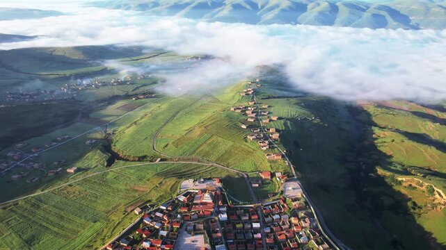 Aerial view of rural village and green hills under low clouds