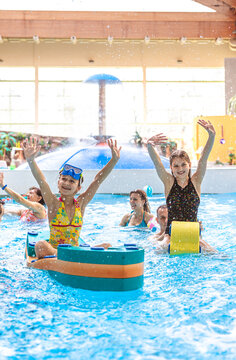 Happy hildren raising hands and playing with pool floats at an indoor water park