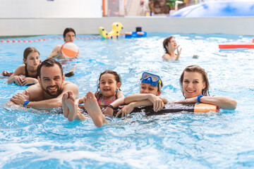 Fototapeta premium Portrait of a happy family smiling and looking at the camera while relaxing with pool floats at an indoor water park
