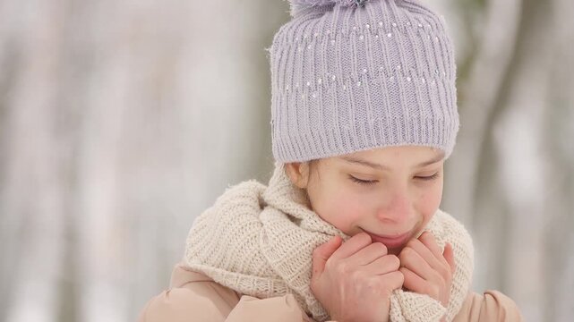 Beautiful girl in jacket and hat with a bright scarf dreaming about something on the background of a winter city park.