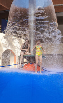 Group of happy people jumping from a blue water mushroom fountain dome at an indoor water park